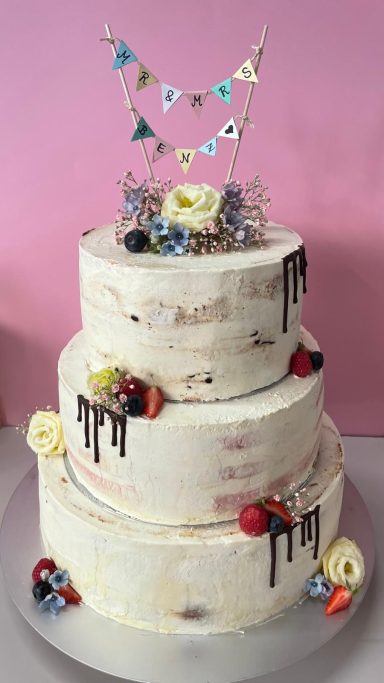 Eine 3-Stöckige Hochzeitstorte mit wenigen Schokoladentropfen am Rand und Blumen, sowie Beeren-Dekoration.