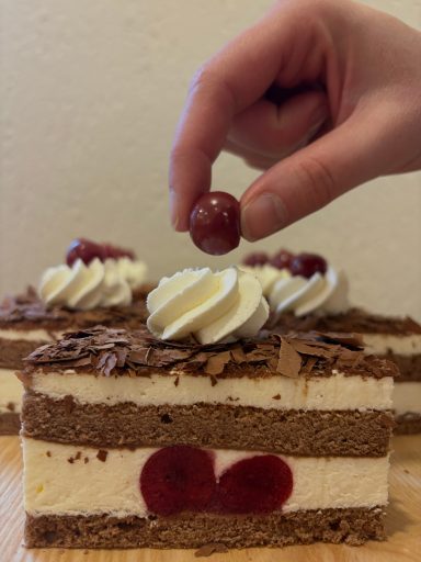 einer Schwarzwälder-Kirschschnitte bei der die Kirsche aufgesetzt wird. 