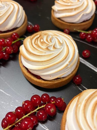 Foto von vier Johannisbeer-Tartelettes mit einer schön gebräunten Baiserhaube,  auf einem schwarz-weißen Untergrund.